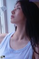 A woman in a white tank top looking out a window.