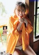 A woman in an orange raincoat posing by a window.