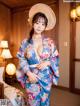 A woman in a blue kimono and a straw hat posing for the camera.