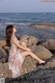 A woman sitting on a rock by the ocean.