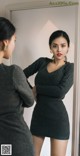 A woman standing in front of a mirror wearing a gray sweater dress.