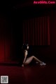 A woman sitting on the floor in front of a red curtain.