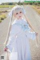 A woman in a white dress standing on a dirt road.