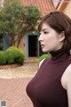 A woman in a brown turtle neck top standing in front of a building.