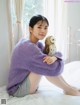 A woman sitting on a bed holding a stuffed owl.