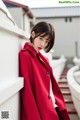 A woman in a red coat leaning against a wall.